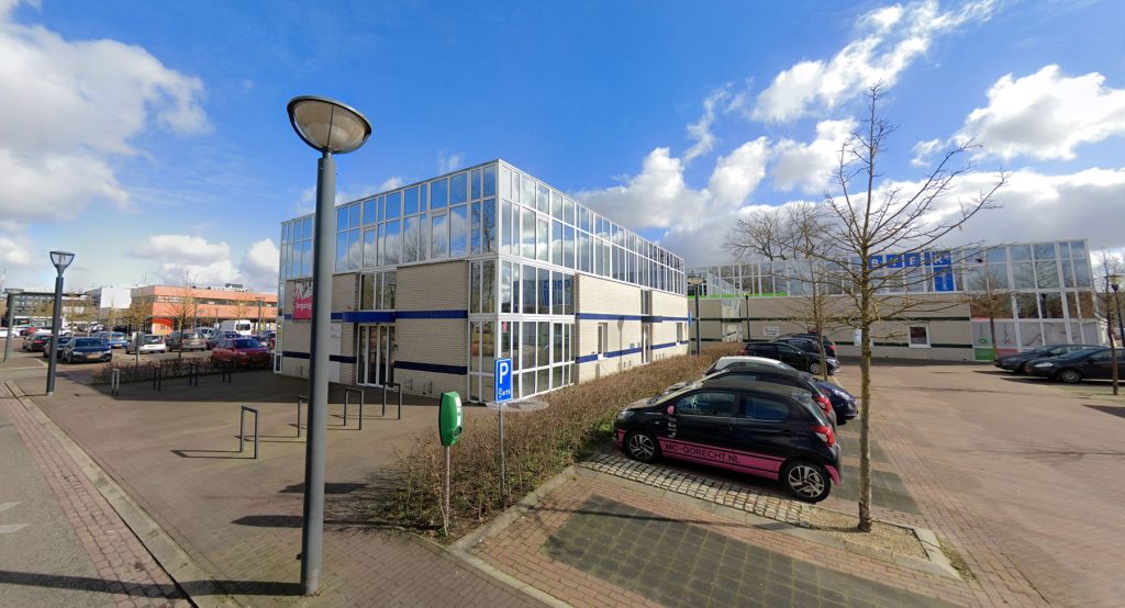 Exterieur van Medisch Centrum Gorecht in Hoogezand; een modern wit gebouw met veel glaspartijen, omringd door een parkeerplaats met een roze bestickerde auto op de voorgrond.
